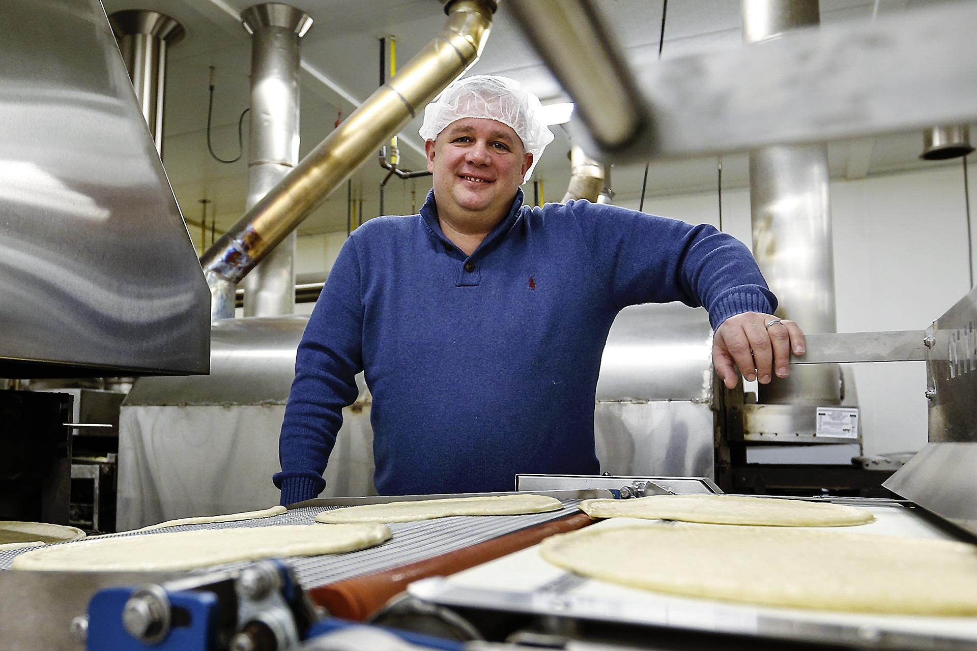 Man in hairnet stands behind pizza-making machine