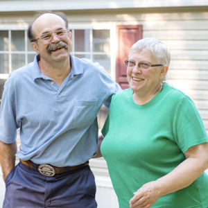 Man and woman, both smiling and standing ouside their manufactured home