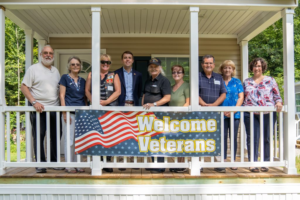 Congressman Chris Pappas poses with the Rock Rimmon board of directors and three veteran homeowners behind a sign that says Welcome Veterans