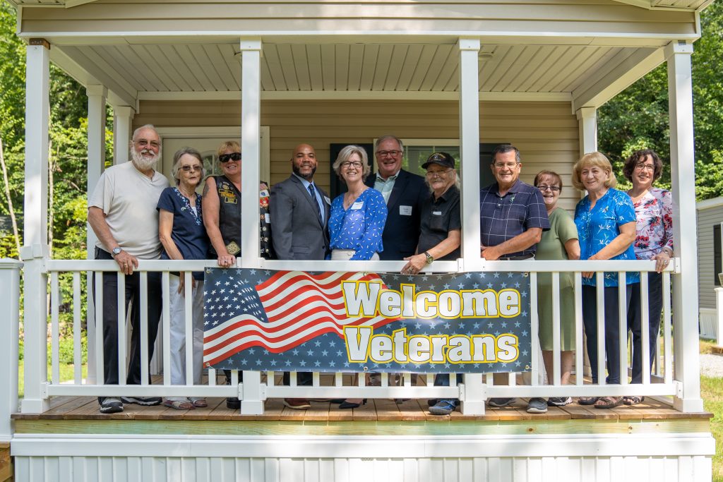 The Rock Rimmon board of directors, three veteran homeowners , and others posed behind a sign that says Welcome Veterans