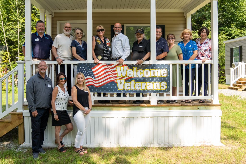 The Rock Rimmon board of directors, three veteran homeowners , and others posed behind a sign that says Welcome Veterans