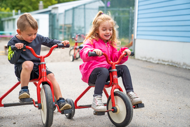 Two children race on their tricycles.